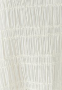 Tessuto bianco trasparente con pieghe verticali raccolte e delicato bordo in pizzo disposto in linee orizzontali, creando un aspetto testurizzato e stratificato.