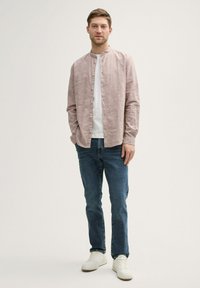 Camisa de manga larga rosa clara con cuello mao, con botones al frente, usada sobre una camiseta blanca. Combinada con jeans azules y zapatillas blancas.