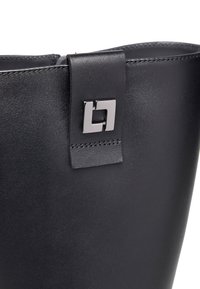 Dettaglio di un boot in pelle nera caratterizzato da un design elegante, chiusura con zip e un accento metallico di forma quadrata nella parte superiore.