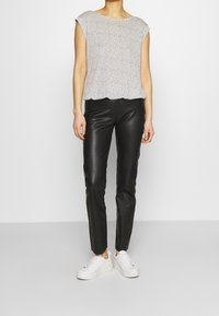 Haut à pois blancs et noirs avec des manches courtes, associé à un pantalon en cuir noir et des baskets blanches, présentant une coupe décontractée et un ourlet en forme de vagues.