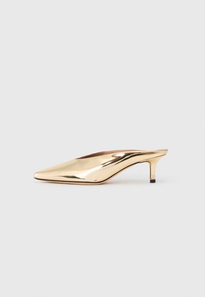 Skinnende gylden mule med spids tå og lav kittenhæl, slip-on stil, vist på en ensfarvet lys grå baggrund.