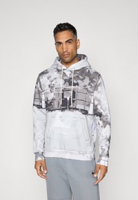 šedá a biela mikina s kamuflážným vzorom, so sťahovacou šnúrkou, prednou kapsou a rebrovanými manžetami. Hladká textúra, zmesová bavlnená látka.