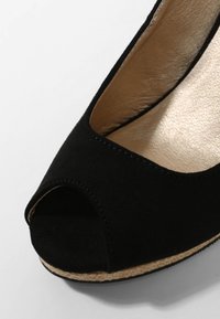 Chaussure compensée en daim noir à bout ouvert avec semelle intérieure en cuir beige et bordure en jute tressée autour de la semelle, photographiée sur une surface claire.