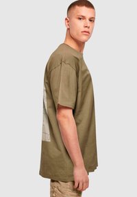 Oliven grøn bomulds t-shirt med en afslappet pasform. Har et puslespilsmønster grafik på ryggen og korte ærmer. Struktureret stof.