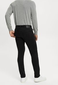 Černé fitted džíny s hladkou texturou, vzadu s kapsami a koženou nášivkou na pase, doplněné světle šedým dlouhým rukávem.