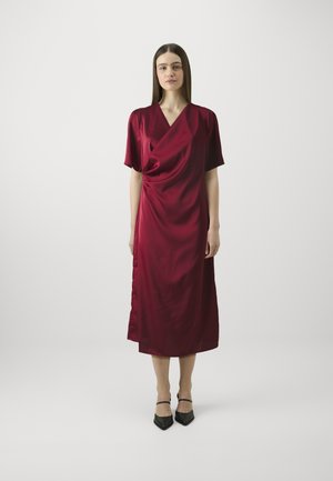Burgundy satin wrap dress with short sleeves, V-neckline, draped front, and mid-calf length. Paired with black strappy heeled shoes.