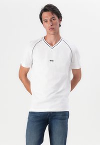 Balta, trumpa V formos iškirptė t-shirt pagaminta iš kvėpuojančios tekstūros audinio, su juodomis detalėmis ir mažu "BOSS" logotipu priekyje.