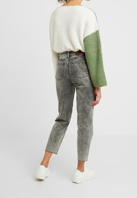 Suéter de punto oversized en crema y verde, jeans de tiro alto grises y zapatillas blancas. Los detalles notables incluyen mangas anchas y textura de mezclilla desgastada.