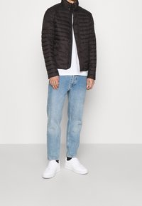 Černá péřová bunda s vysokým límcem, horizontálním prošíváním a patentkami. V kombinaci se světle modrými džíny a bílými teniskami.