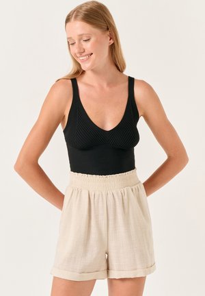 Zwarte geribbelde bodysuit met een diepe V-hals, gecombineerd met beige linnen shorts met een gerimpelde taille en opgerolde zoom.
