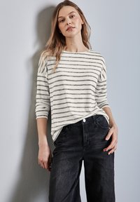 Wit en grijs gestreepte lange mouw top, gedragen met donkere jeans. De top heeft een relaxte pasvorm met een bootnek en opgerolde mouwen.