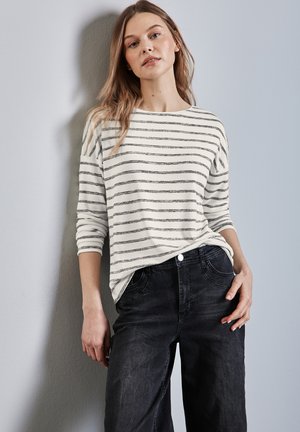 Maglietta a maniche lunghe a righe bianca e grigia abbinata a jeans scuri. La maglietta ha una vestibilità rilassata con scollo a barca e maniche arrotolate.