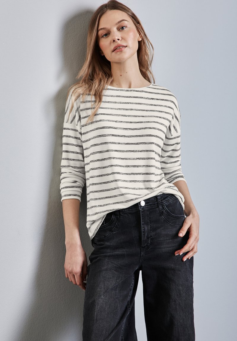 Wit en grijs gestreepte lange mouw top, gedragen met donkere jeans. De top heeft een relaxte pasvorm met een bootnek en opgerolde mouwen.
