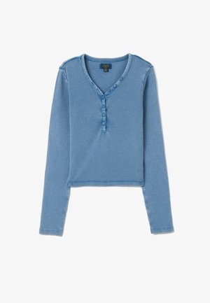Maglietta henley blu a maniche lunghe con vita a V, patta con tre bottoni e design crop. Tessuto morbido e silhouette aderente.