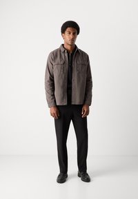 Chaqueta de mezcla de algodón gris con dos bolsillos en el pecho, camiseta negra con cremallera, pantalones negros y zapatos negros, con una textura suave y un corte relajado.