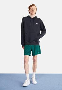 Sweatshirt à capuche gris foncé, associé à un short en maille verte. Le sweatshirt a une poche sur le devant et un petit logo ; le short a une taille élastique.