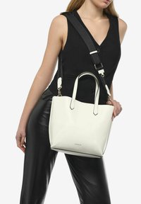 Witte leren handtas met korte handvatten en een afneembare schouderriem, met een gladde textuur en een minimalistisch ontwerp.