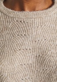 Maglione marrone chiaro lavorato a maglia con motivo ondulato e strutturato. Il collo è a girocollo a coste, che esalta la morbidezza complessiva.