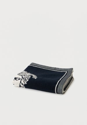 Serviette noire et grise pliée avec un motif de tête de Méduse blanche sur un fond blanc uni.