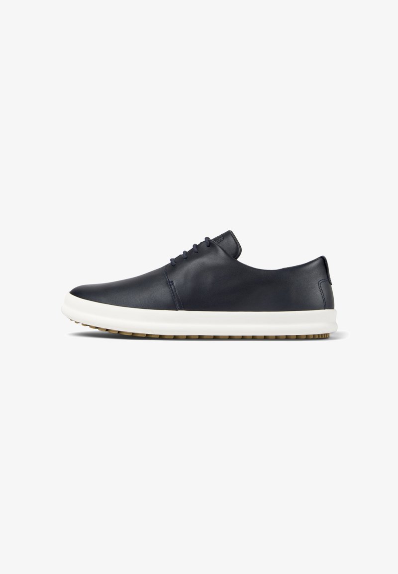 Zapatillas de deporte de cuero azul marino con un acabado suave, suela de goma blanca y suela exterior beige en contraste; cuenta con seis ojales y una punta redondeada.