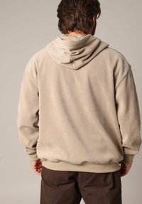 Beige corduroy hoodie met een losse pasvorm, voorzien van een grote capuchon en geribbelde manchetten. Naaddetails op de rug voegen textuur toe.