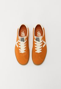 Orange canvas sneakers with white laces, featuring a rubber sole and contrasting white logo on the side. Smooth texture and classic design.