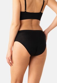 Sous-vêtement en coton noir avec une coupe taille haute, doté d'une ceinture festonnée et d'une texture lisse, vu de dos.