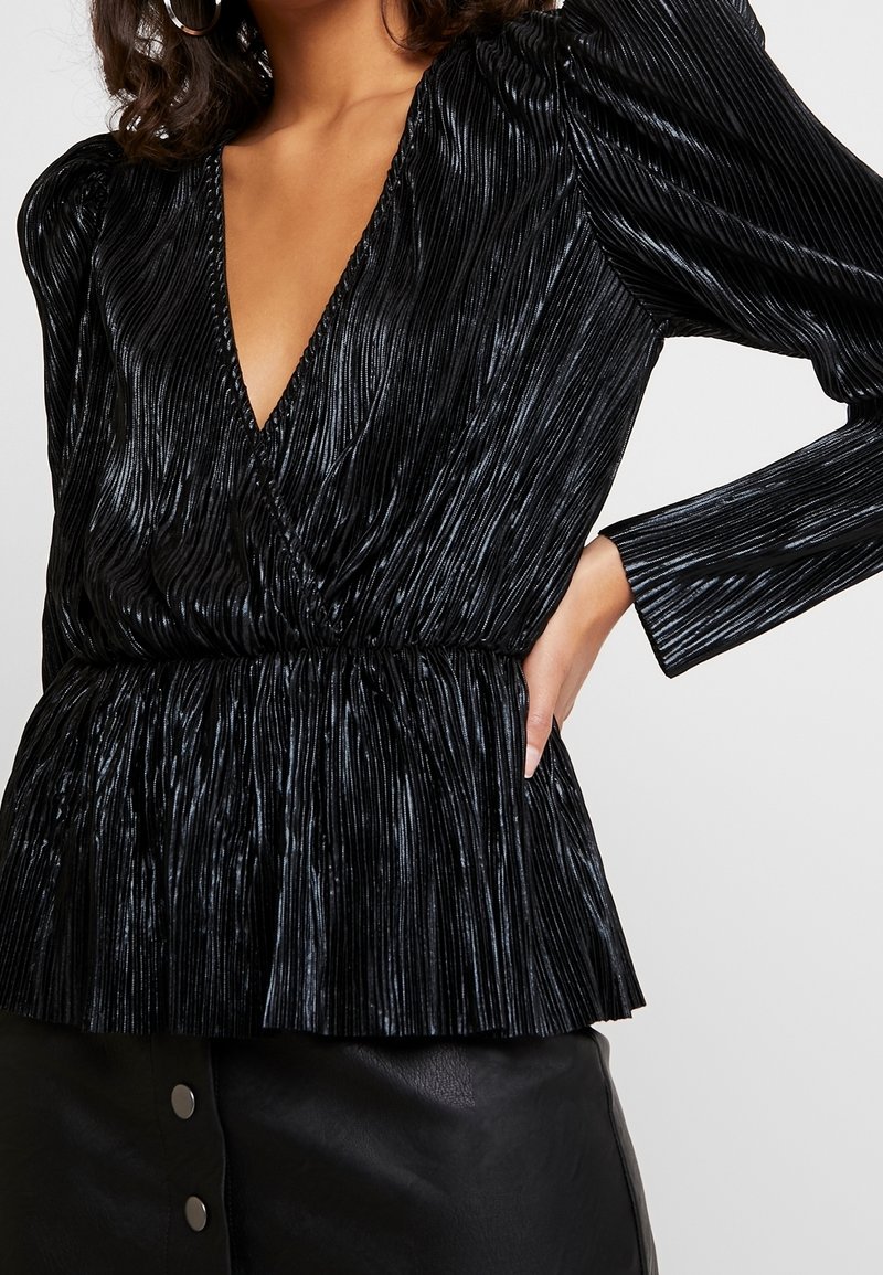 Svart plisserad topp med djup V-ringning, långa ärmar och insvängd midja. Tyget har en glänsande, texturerad yta som skapar vertikala linjer.