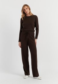 Bruin, gebreide trui en bijpassende joggingbroek met trekkoord. Zachte textuur, geribde manchetten, relaxte pasvorm, gecombineerd met witte sneakers.