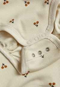 Crème ribbel babyromper met oranje kersenprint en drukknopen langs de onderrand.