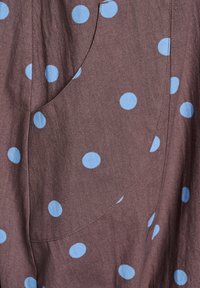 Brauner Stoff mit großen blauen Punkten und einer sichtbaren Tasche, zeigt eine glatte Textur und ein lässiges Design.