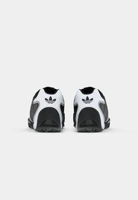 Black and white athletic shoes with a smooth leather upper, textured panels, and a distinctive logo on the heel. Rounded toe and rubber outsole.