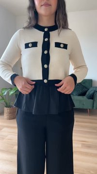 Suéter de malha preto e creme com design peplum, apresentando botões metalizados e detalhes pretos nos bolsos e punhos.