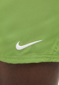 Vihreät urheilushortsit, joissa on tekstuuri pinta ja valkoinen brodeerattu Nike-logo helman kohdalla.