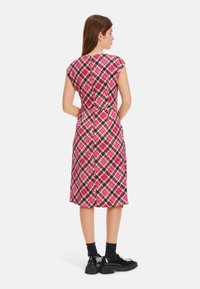 Knieumhangkleid in einem geometrischen Muster aus Pink, Schwarz und Creme. Kurze Ärmel, tailliert und mit glatter Stofftextur.