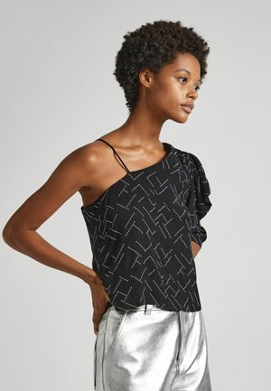 Top asimmetrico nero con una spallina, caratterizzato da un motivo geometrico bianco. Il tessuto ha una consistenza liscia; abbinato a pantaloni metallici argento.