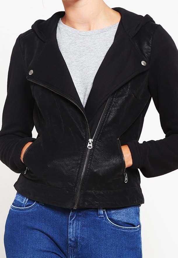 Giacca da motociclista nera con una texture simile alla pelle, chiusura frontale con zip, bottoni a pressione e cappuccio, abbinata a una maglietta grigia e jeans blu.