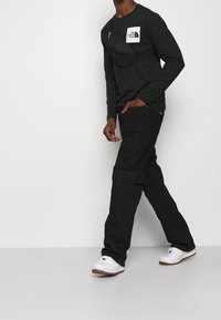 Svart långärmad skjorta med bröstficka, i kombination med svarta cargo-byxor med flera fickor, och vita sneakers med bruna sulor.