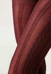 Collants tricotés bordeaux présentant un motif texturé avec des câbles diagonaux et des sections lisses, conçus avec une finition douce et semi-opaque.