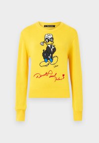 Pull en tricot jaune avec Donald Duck, vêtu d'une veste noire, de chaussures bleues et d'un détail signature rouge. Col rond et poignets côtelés.