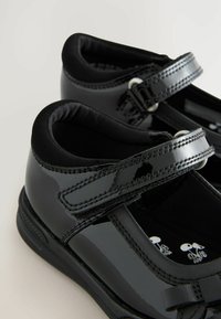 Chaussures en cuir verni noir avec un bout arrondi, une sangle avec quincaillerie métallique, un intérieur rembourré et une semelle texturée.