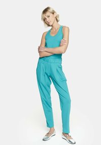 Turkusowy top bez rękawów w zestawieniu z pasującymi plisowanymi spodniami. Strój ma luźny krój i miękką fakturę. Całość uzupełniają srebrne baleriny.