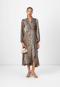 Løveprint omslagskjole med lange ærmer, silkeagtig tekstur og asymmetrisk kant. Brune og beige farver, parret med en lille beige håndtaske.