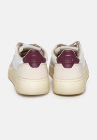Baskets blanches et beiges avec une tige en cuir lisse, un talon en daim et des accents bordeaux. Elles possèdent une semelle en caoutchouc épaisse et des détails cousus.