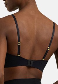 Svart bh med tunna remmar och guldhardware. Har ett hakhäng i ryggen. Slät textur med en enkel, minimalistisk design.