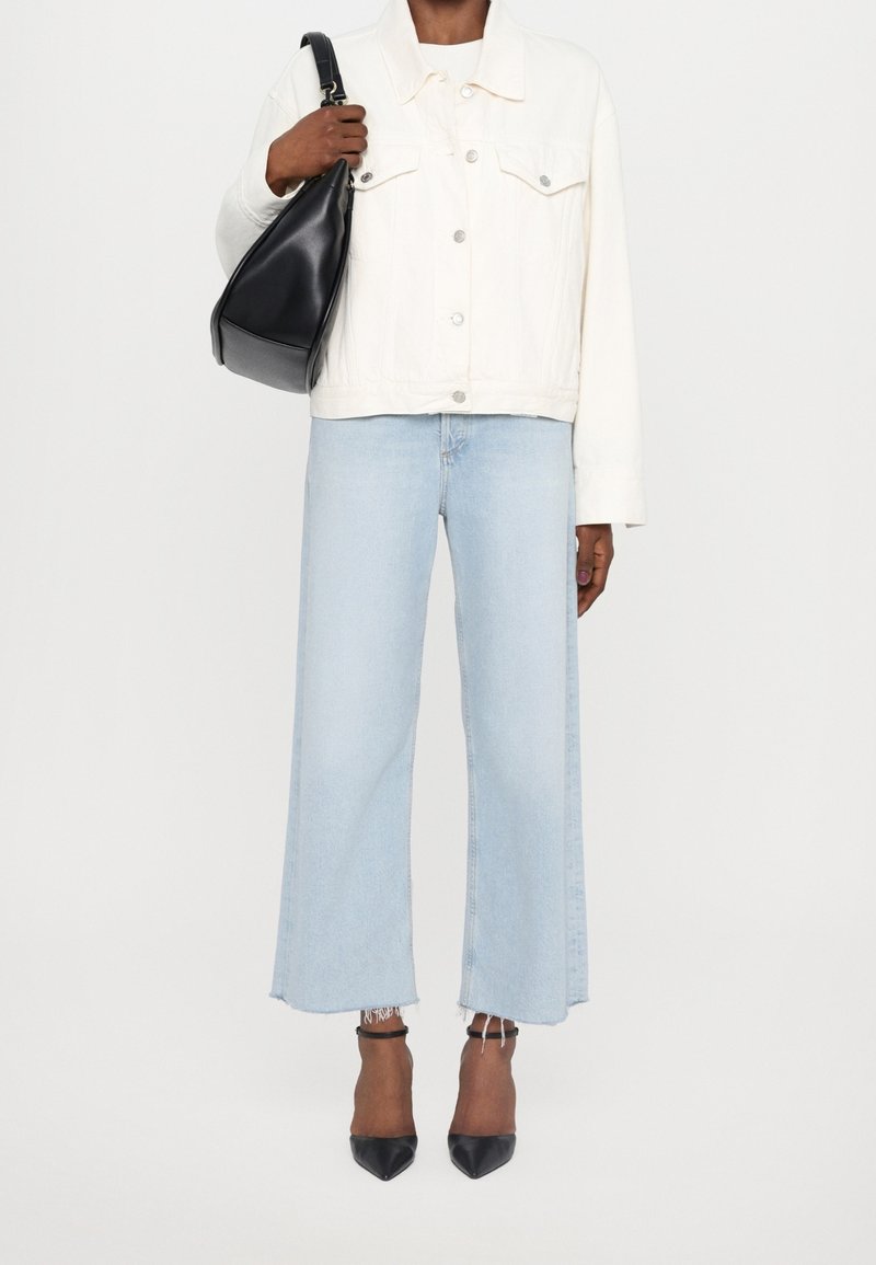 Vit denimjacka med en kortad passform, kombinerad med ljusblå vida jeans. Svarta slingback-klackar och en svart läderaxelväska.