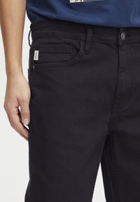 Vaqueros de mezclilla negra con una textura suave, que presentan un bolsillo frontal, una pequeña etiqueta en la cinturilla y un corte clásico.