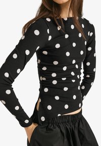 Černý dlouhý rukáv z měkké látky, zdobený bílými puntíky, úzký střih, s nařasenými boky a zakřiveným spodním lemem. Doplněno černými šortkami.