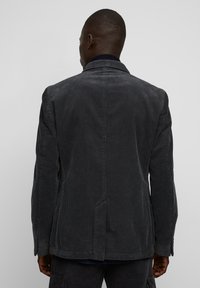 Blazer in corduroy grigio scuro con una vestibilità su misura, spacco singolo sul retro e polsini con bottoni. Tessuto strutturato con righe verticali.