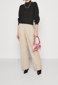 Osoba w czarnym swetrze, beżowych szerokich spodniach, czarnych butach na obcasie i trzymająca małą różową torbę na ramię z złotymi akcentami.